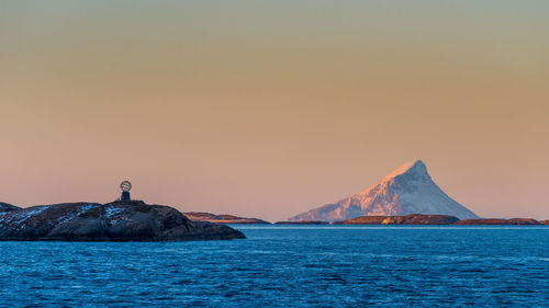 Lighthouse by sea against clear sky during sunset