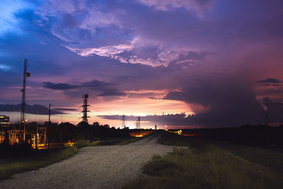 Road amidst field against sky during sunset