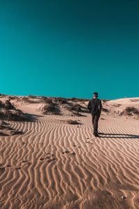 Rear view of man walking on sand dune in desert against clear blue sky