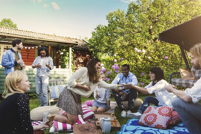 Happy woman serving food to friends in backyard during summer party