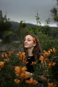 Young woman with flowers on field against sky