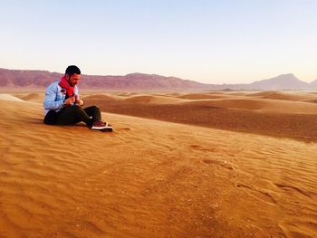 People sitting on desert against clear sky