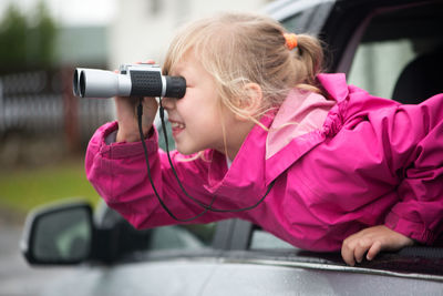 Sid view of girl looking through binoculars while traveling in car