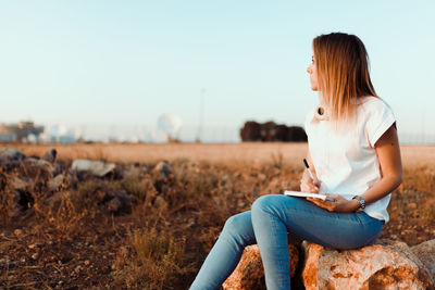 Woman sitting on field against clear sky