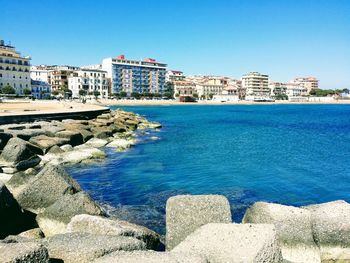 Buildings by sea against blue sky