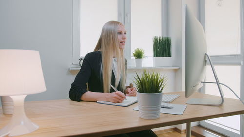 Businesswoman writing in book while looking at computer at office