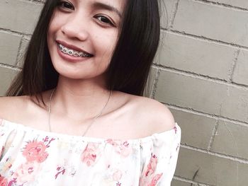 Portrait of smiling young woman with braces standing against brick wall