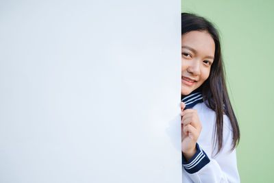 Portrait of a smiling young woman standing against wall