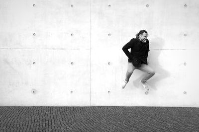 Full length of happy man jumping over footpath against wall