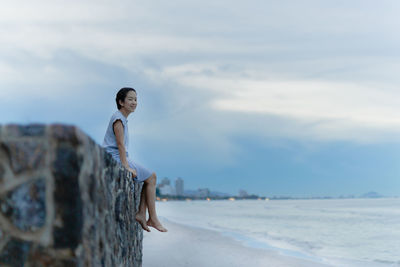 Portrait of young man standing on rock at beach against sky