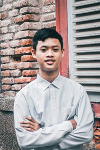 Portrait of young man standing against brick wall