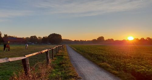 Road amidst field against sky during sunset