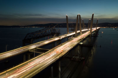 Light trails on bridge over river against sky at night