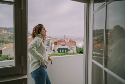 Woman standing by window against sky