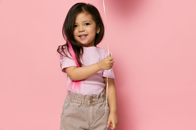 Portrait of young woman standing against pink background