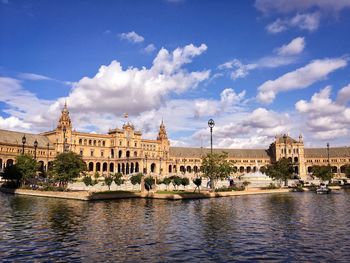 View of buildings by river against cloudy sky