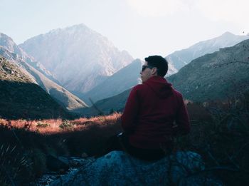 Rear view of man sitting on mountain against sky
