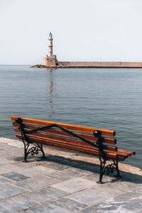 Empty bench by sea against clear sky