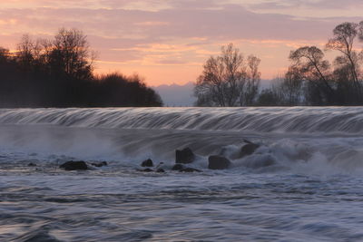 Scenic view of waterfall against sky at sunset