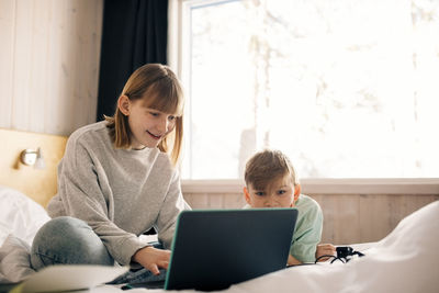 Smiling girl with brother using laptop in bedroom at home