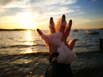 Cropped hand of woman with soap sud at beach against sky during sunset