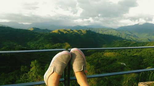 Low section of man relaxing on mountain against sky