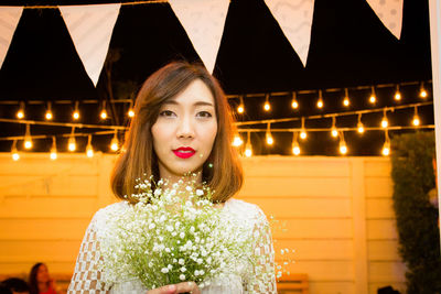 Portrait of woman with bouquet against illuminated decoration at night