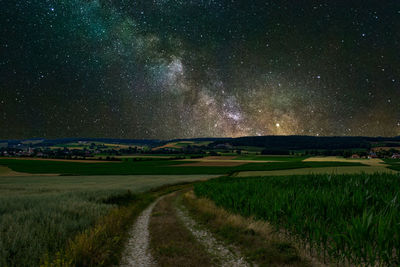 Empty footpath amidst grassy field against star field