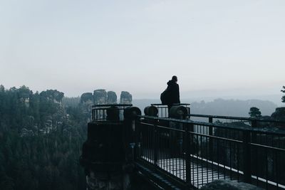 Silhouette man standing on railing against clear sky