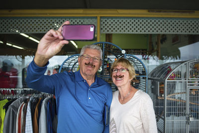 Senior couple wearing artificial mustaches taking selfie with smart phone in store