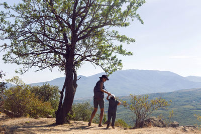 Mom and son stand on a mountain next to a tree in the summer in the crimea