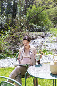 Pregnant woman reading newspaper while sitting on chair in yard