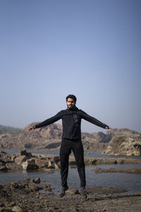 Young athletic man doing burpee near a lake surrounded with mountains early in the morning.