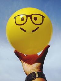 Close-up of woman holding yellow ball against sky