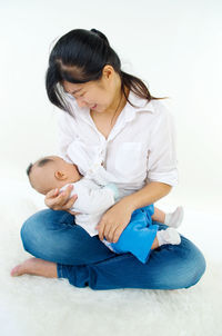 Full length of mother breastfeeding baby against white background