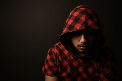 Close-up of man wearing checked pattern hooded shirt against black background