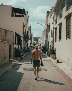 Rear view of man walking on street amidst buildings in city
