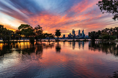 Scenic view of lake by buildings against sky during sunset