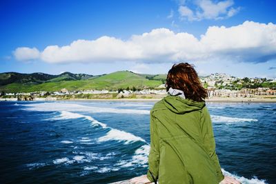 Rear view of woman standing by river against cloudy sky