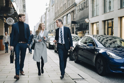 Businesswoman with male colleagues walking on sidewalk in city