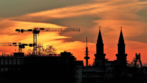 Silhouette crane by building against sky during sunset