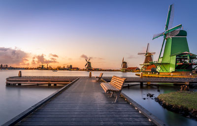 Traditional windmill by sea against sky during sunset
