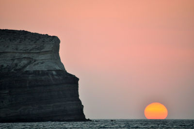Rock formation in sea against clear sky during sunset