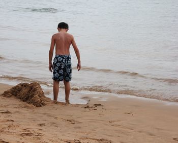 Rear view of shirtless boy standing on beach