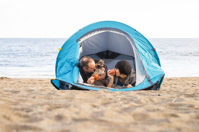 Mature couple and dog in tent at beach against sea