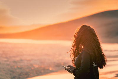 Side view of woman standing on beach during sunset 