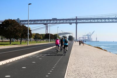 People riding bicycle on bridge in city against sky