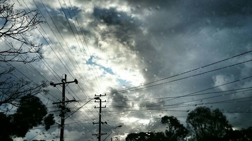 Low angle view of electricity pylon against cloudy sky