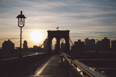 Street light on brooklyn bridge in city against sky during sunset