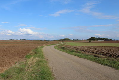 Road passing through agricultural field against sky